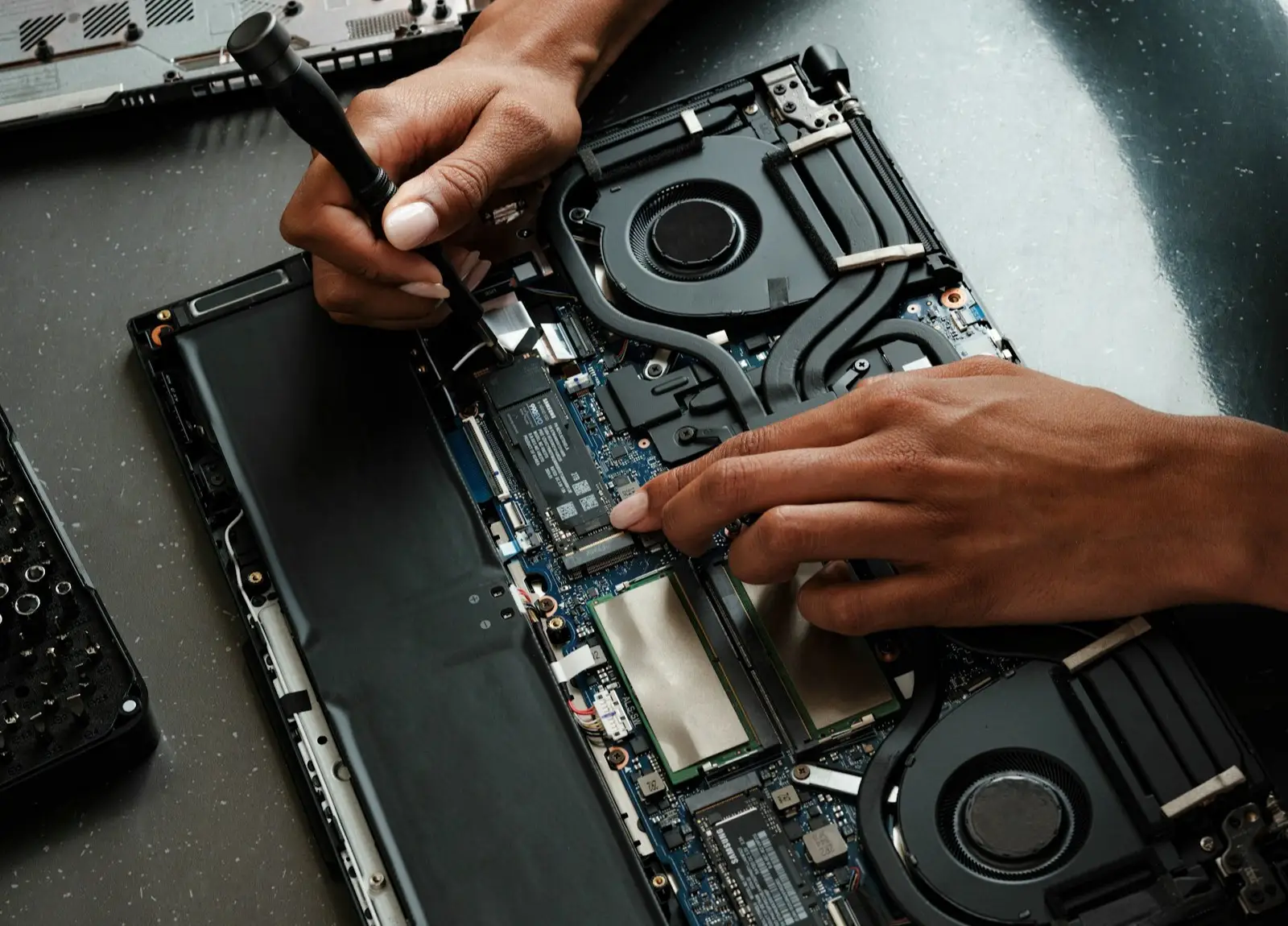 A technician with a screwdriver inside an opened laptop, RAM and SSD exposed